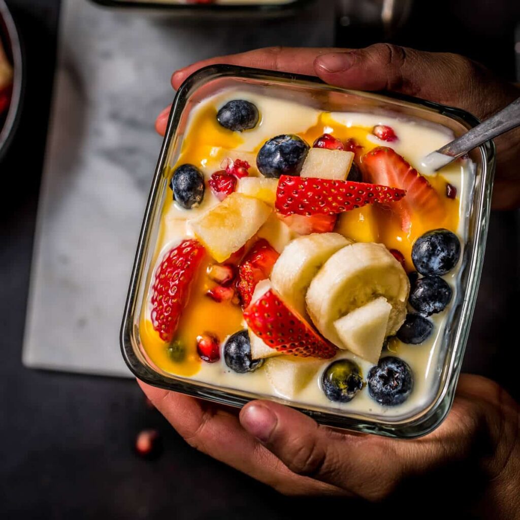 An overhead shot of a child holding a bowl of fruit custard. Another bowl is placed on a marble board.