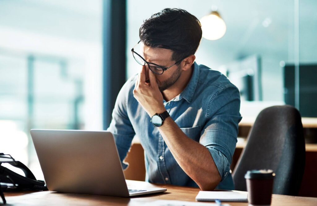 An exasperated man sits in front of his work laptop