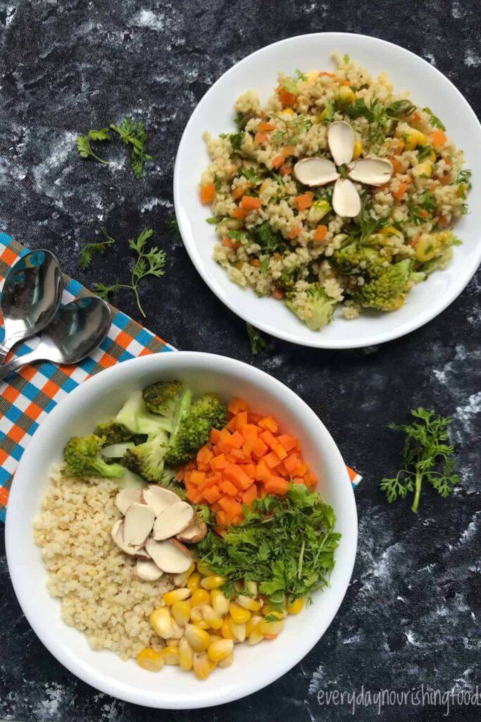 A colorful millet salad served with steamed broccoli, carrots, and corn, topped with fresh herbs, presented in a white bowl on a wooden table.