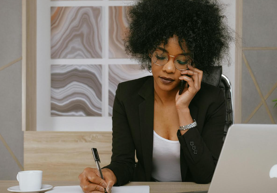 African American Woman with Short Hair and Glasses Talking on a Smartphone and Sitting at a Desk